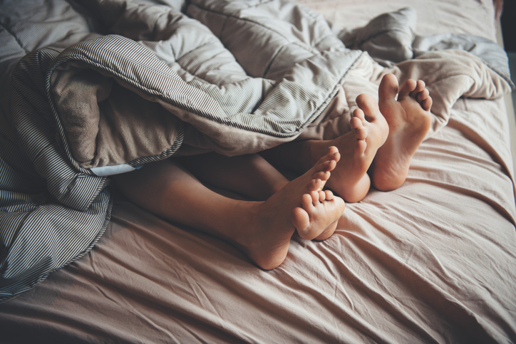Close up photo of feet covered by a quilt of a caucasian couple lying in bed