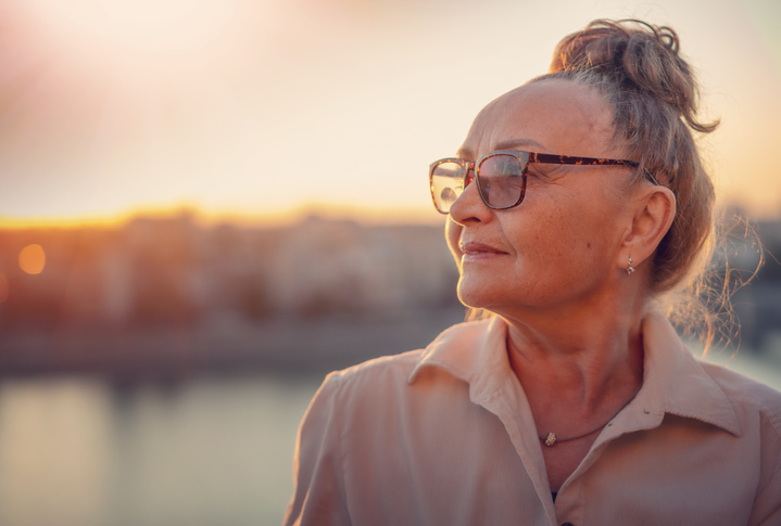 Close up portrait of stylish beautiful mature senior woman wearing glasses 60 years old looking to the side in sunset light