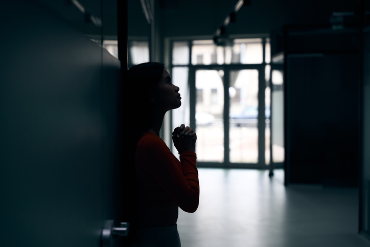 Despondent company employee praying in dark empty office corridor